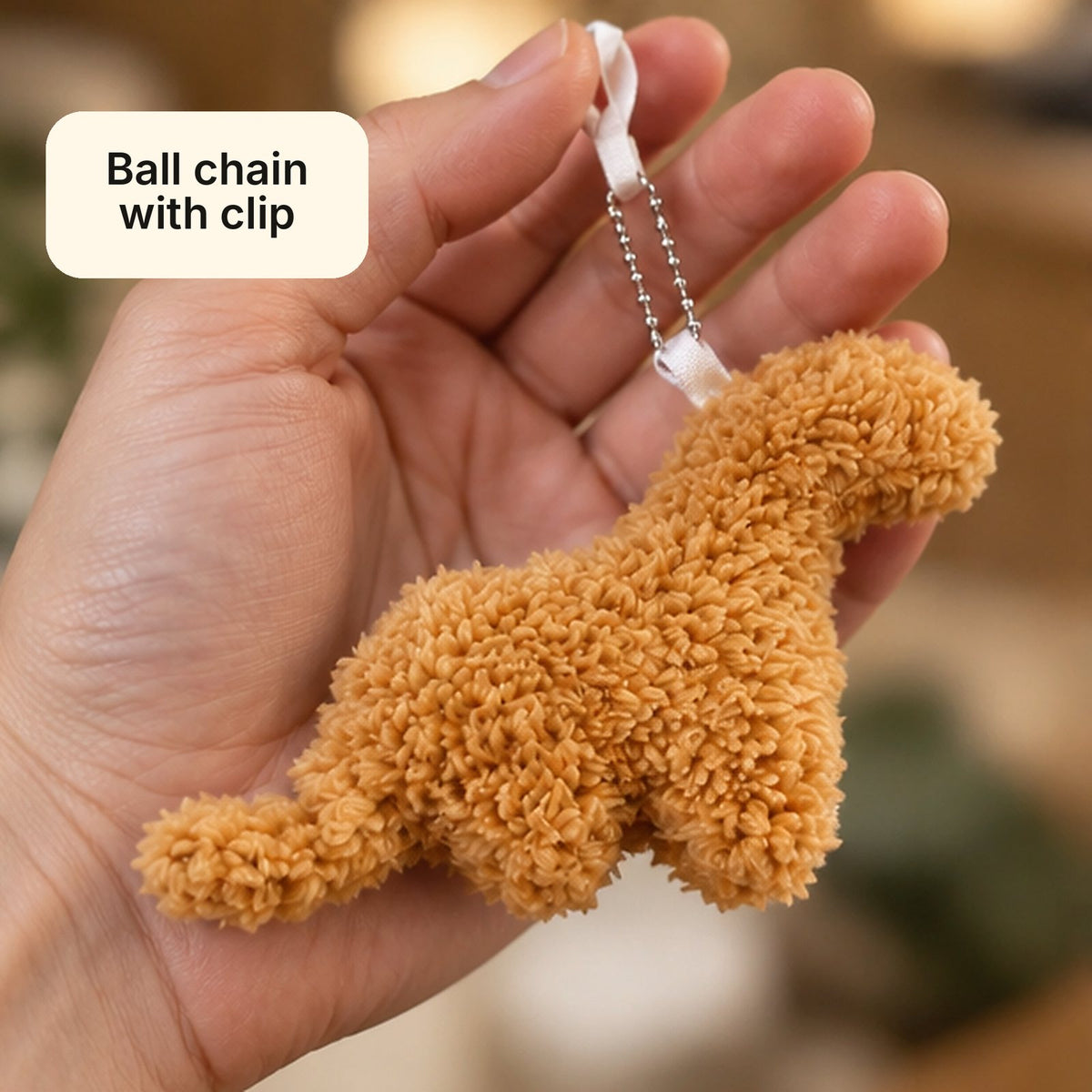 Hand holding a dino nugget plush keychain by its ball chain with clip